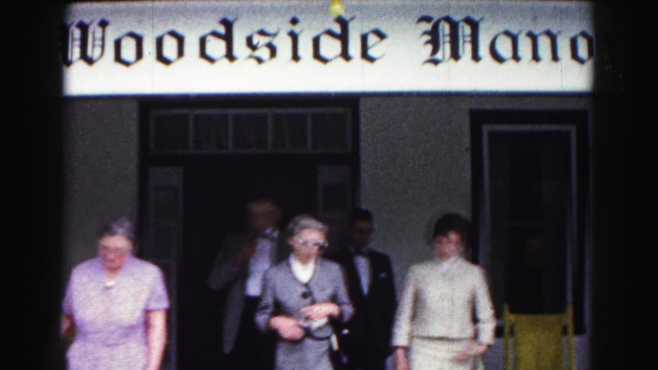 Adults in formal 1960s clothing walk out from Woodside Manor in Hagerstown, Maryland, with the venue sign above them.