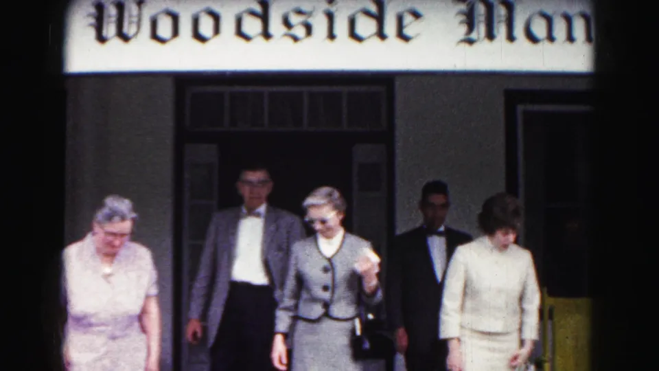 A formally dressed group exits Woodside Manor in 1963 Hagerstown, including women with handbags and men in jackets.