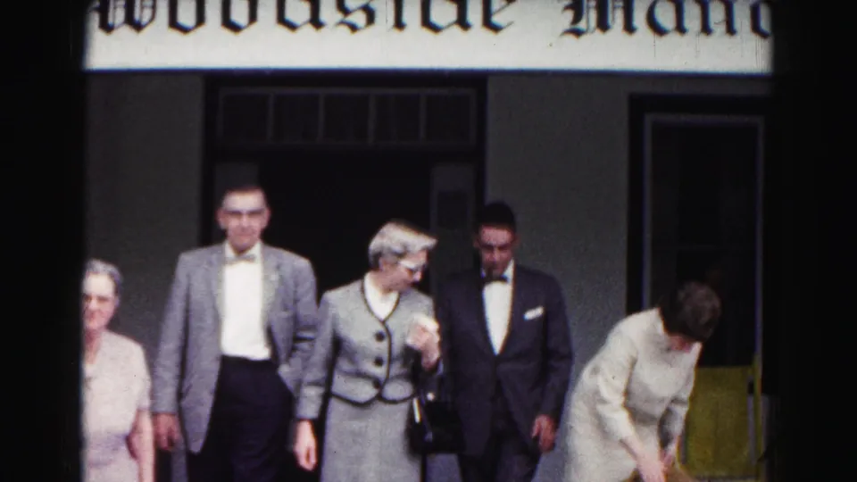 Formally dressed adults pass the Woodside Manor entrance in Hagerstown, Maryland, near the end of the short 8mm clip.