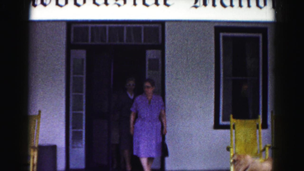 1963 Hagerstown home-movie frame showing a woman in a purple dress stepping out of Woodside Manor with yellow porch chairs nearby.