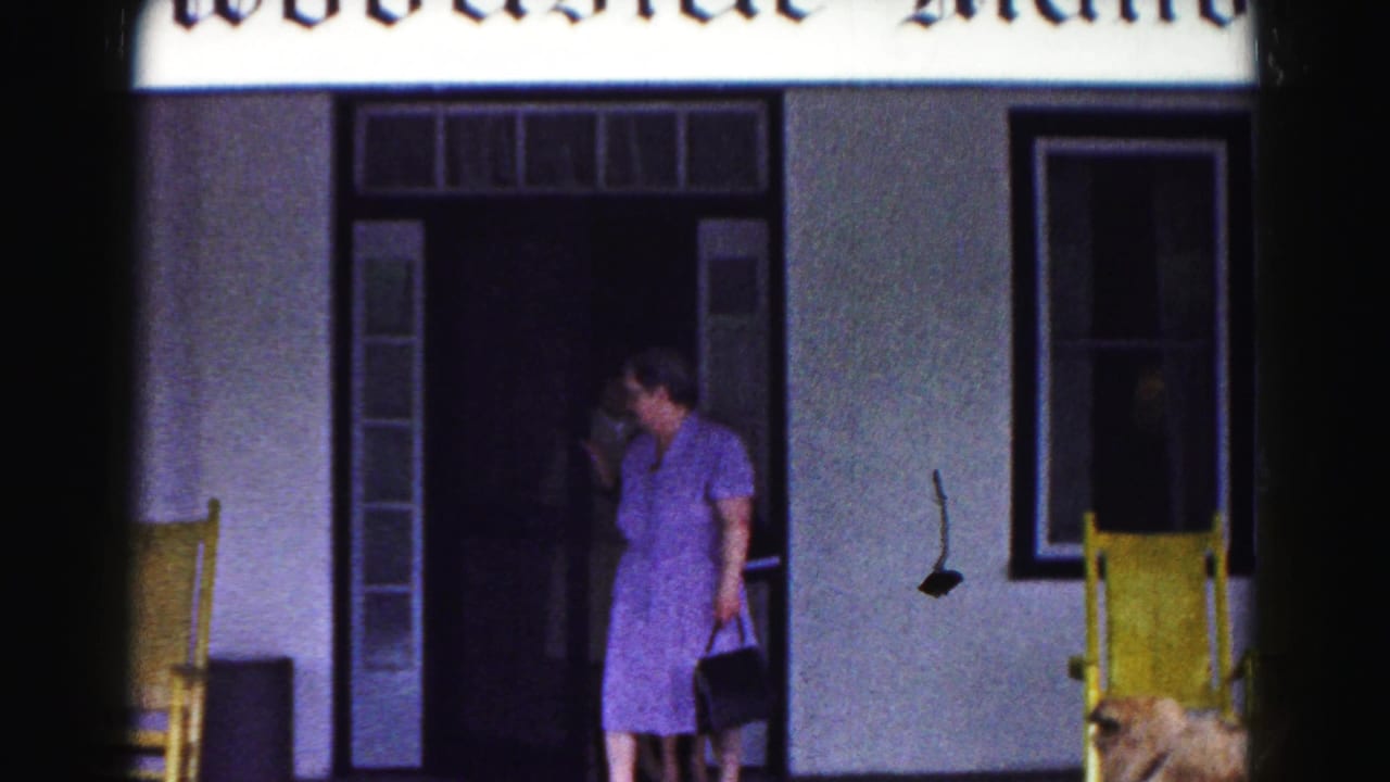 A woman in a purple dress pauses outside the Woodside Manor entrance in Hagerstown, with yellow porch chairs and a window behind her.