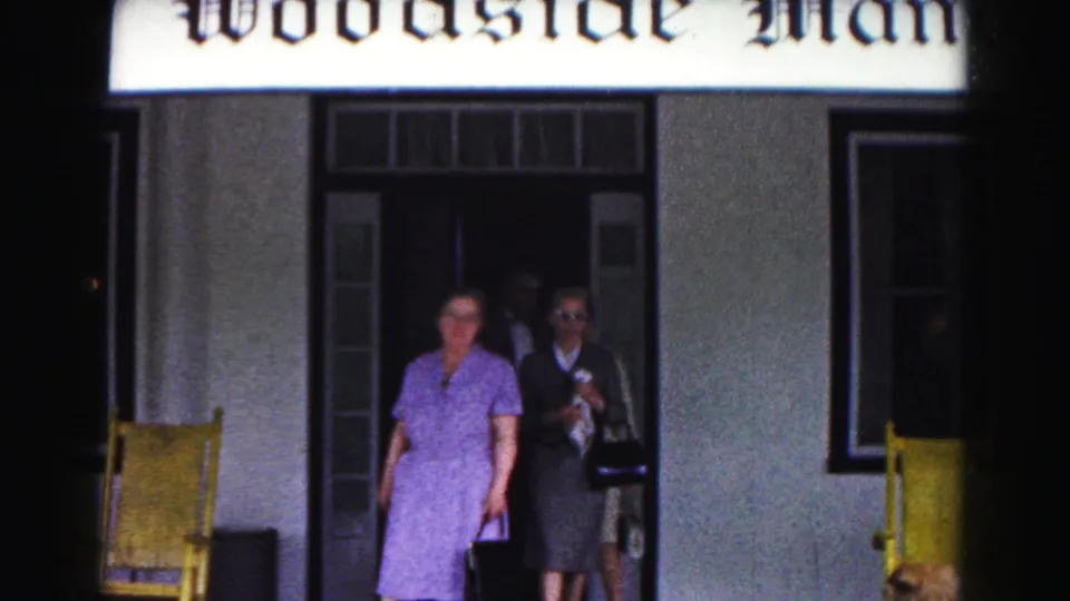 Women leave the dark Woodside Manor doorway in a 1963 Hagerstown home-movie frame, led by a woman in a purple dress.