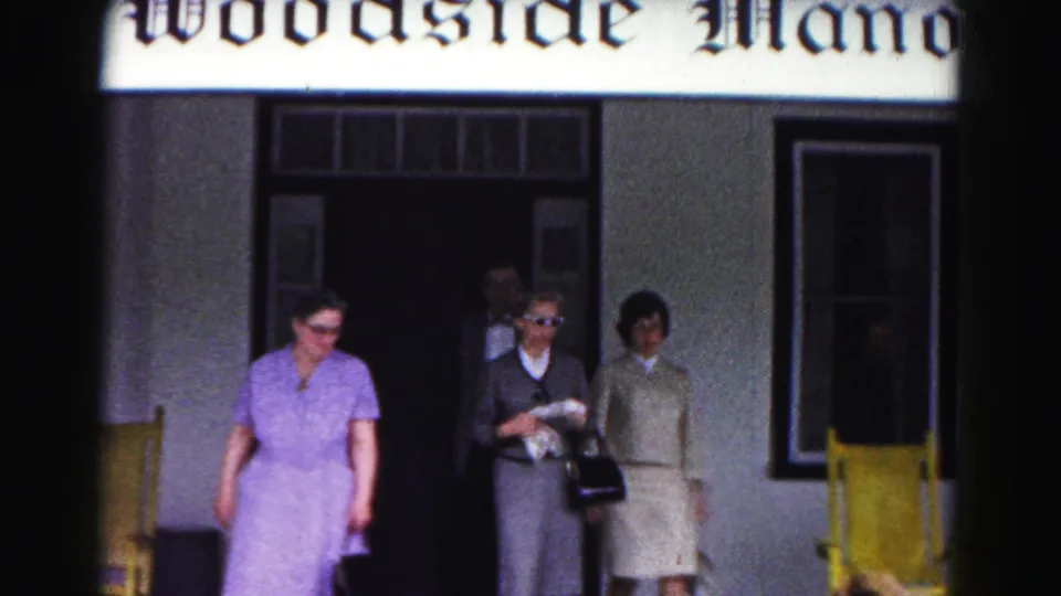 Three women in period dresses walk out from Woodside Manor in Hagerstown, Maryland, with yellow porch chairs framing the entrance.