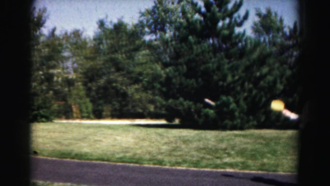1963 Hagerstown-area home-movie frame showing a lawn, road edge, and trees with dark film-frame borders.