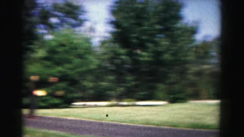 A motion-blurred 1963 Hagerstown outdoor play frame shows grass, trees, paved ground, and a small ball near the lower edge.