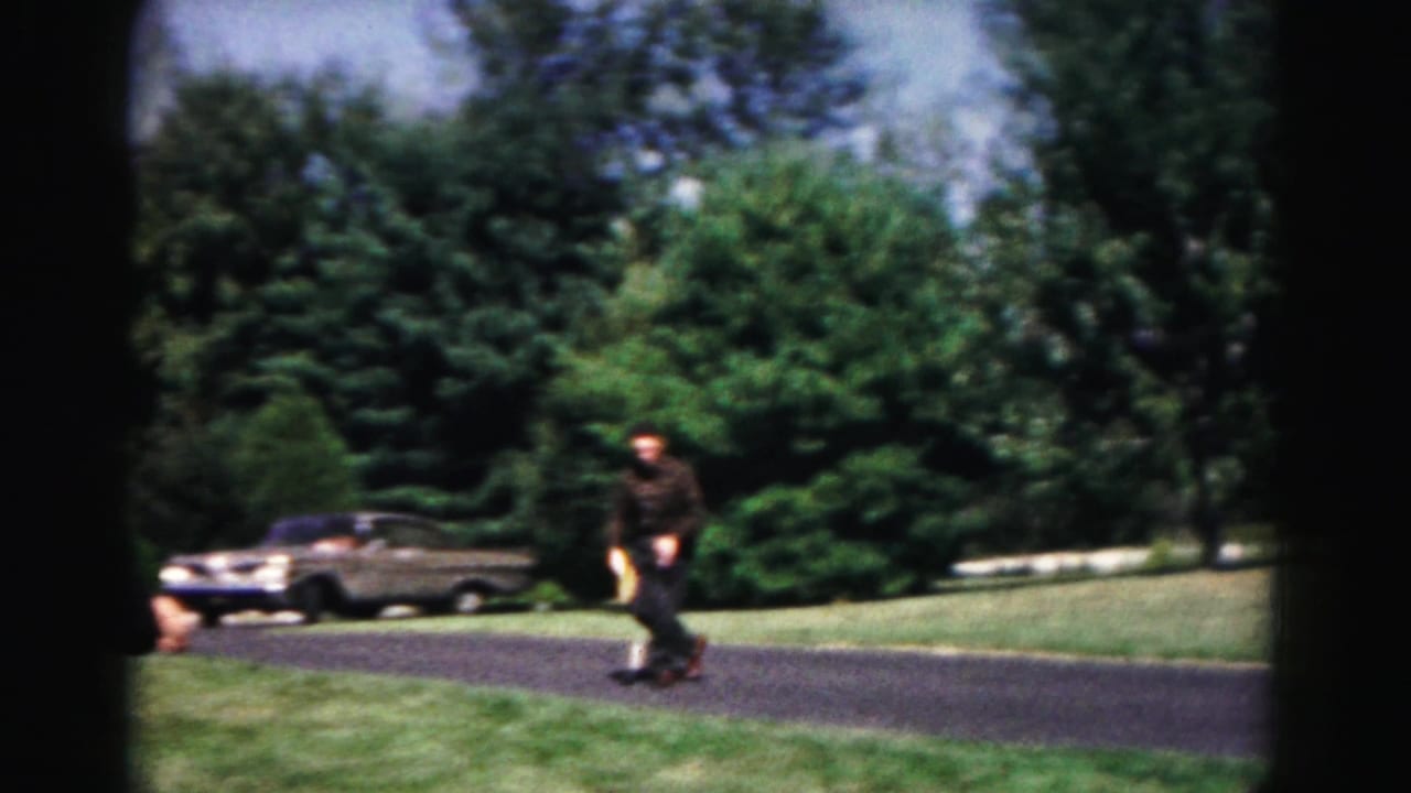 A man in dark clothing holds a paddle on a Hagerstown park path, with a classic car and trees visible behind him.