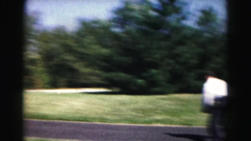 Motion blur shows the white-shirted player moving across a grassy Hagerstown park scene beside the paved path.