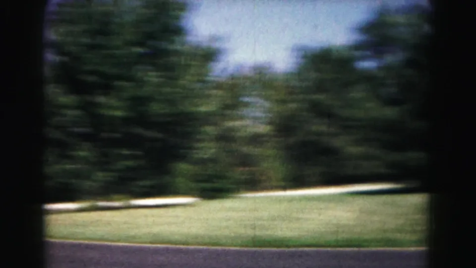 The frame drifts across the Hagerstown park landscape, showing grass, a paved path, and dense trees in soft 8mm blur.