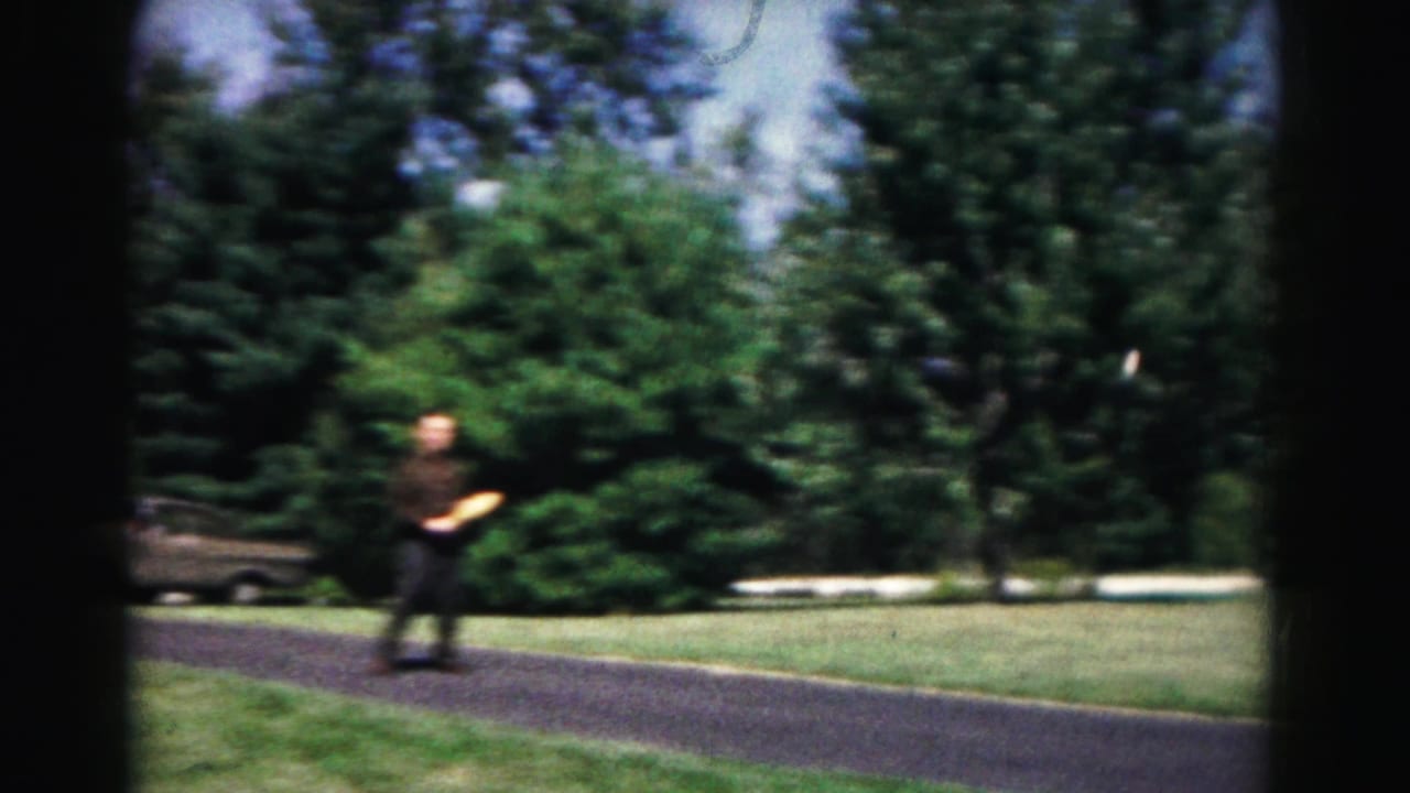 A man in dark clothing appears across a park path in Hagerstown, Maryland, with trees, grass, and a parked car partly visible nearby.