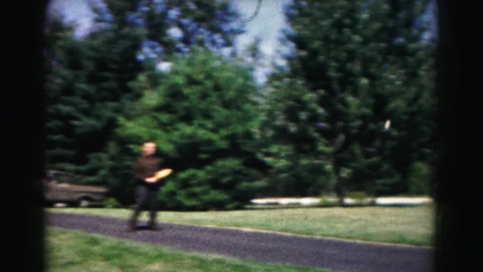 A man in dark clothing appears across a park path in Hagerstown, Maryland, with trees, grass, and a parked car partly visible nearby.