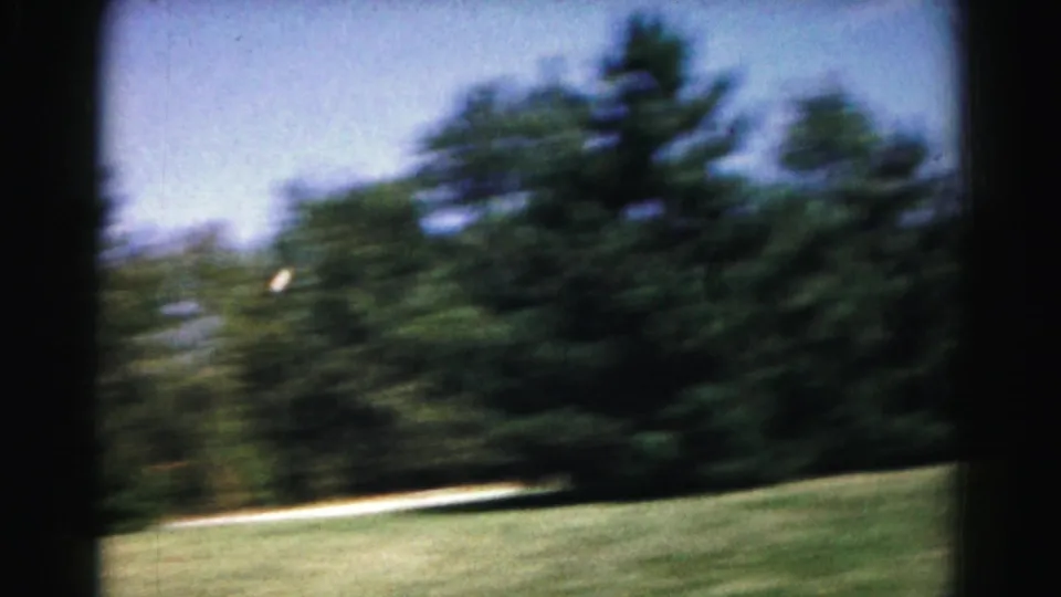 A blurred 8mm frame shows the lawn and tree line during the 1963 backyard tennis scene in Hagerstown.