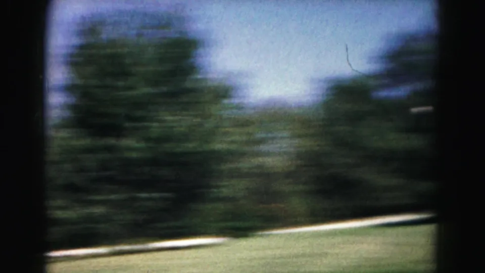 Motion-blurred 8mm frame from the yard game, with trees, blue sky, lawn, and driveway edge visible.