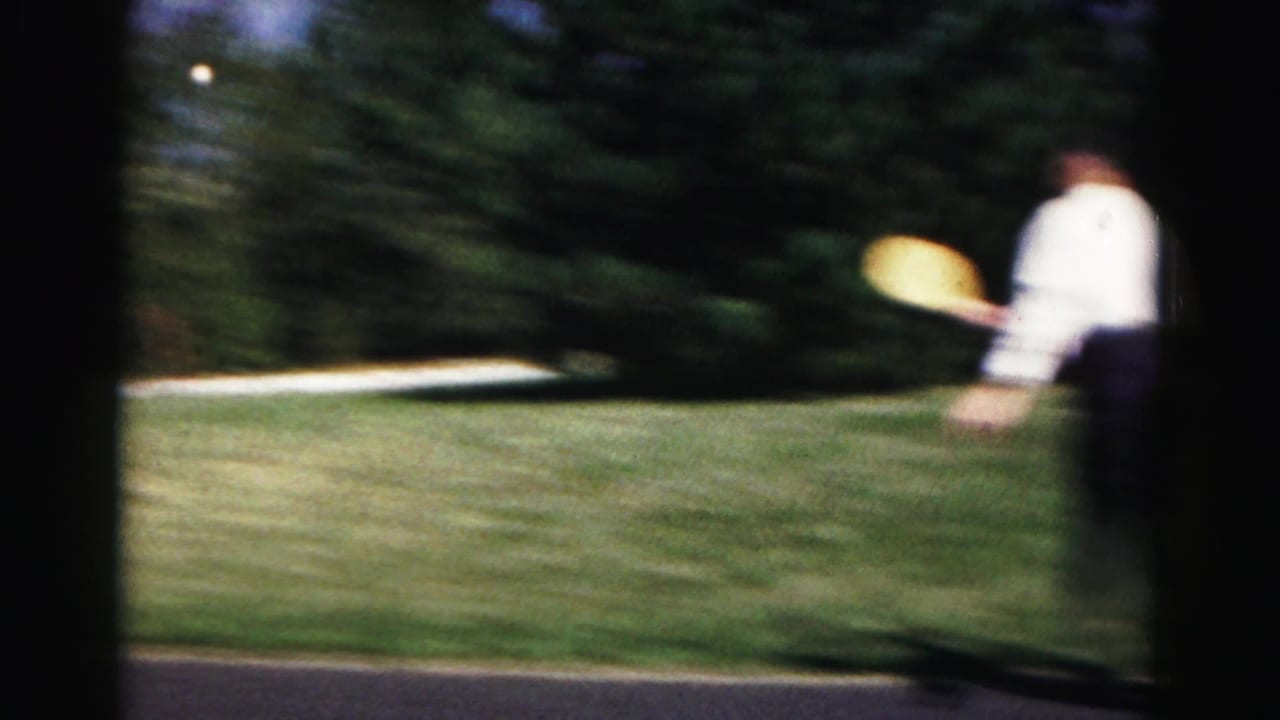 Blurred view of a person holding a yellow disc near a grassy driveway.