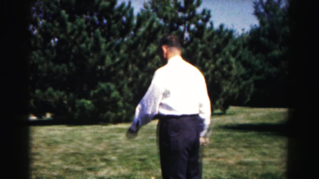 In 1963 Hagerstown, Maryland footage, a man in a white shirt crosses a suburban lawn bordered by trees.