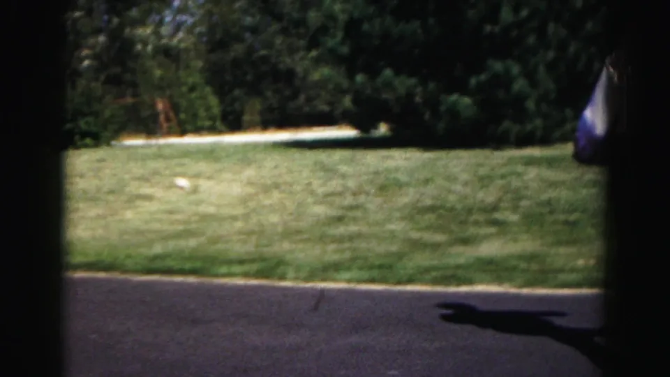 The camera catches the suburban lawn and driveway as a player moves partly out of frame during the paddleball game.