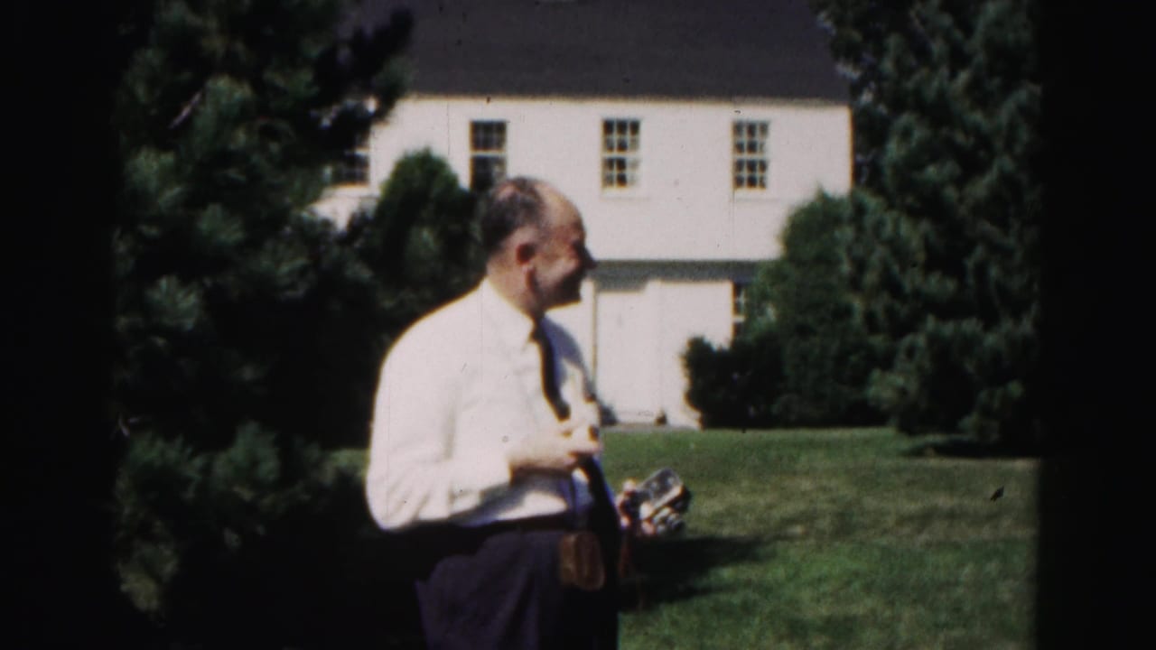 A man in a white shirt and tie turns sideways on a Hagerstown lawn, holding a small object with the white house behind him.