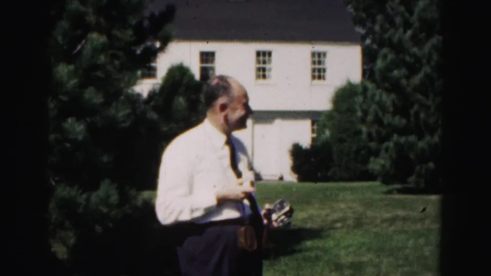 A man in a white shirt and tie turns sideways on a Hagerstown lawn, holding a small object with the white house behind him.