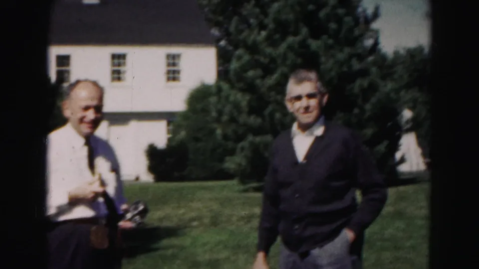 Two men stand near the camera on a Hagerstown residential lawn, with a white house and trees visible in the 1963 8mm frame.