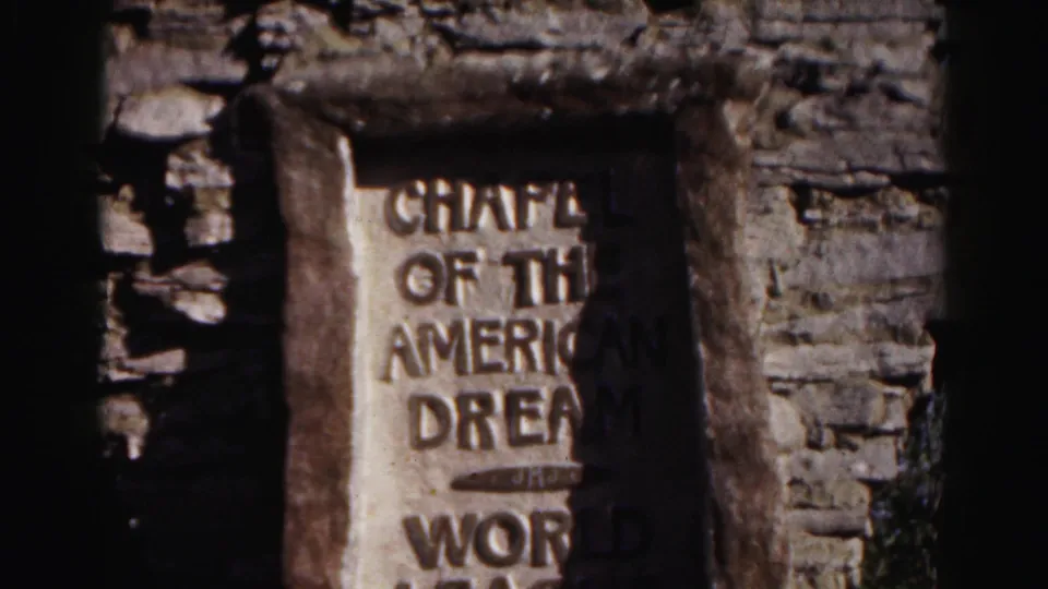 1963 Hagerstown home-movie frame showing a weathered plaque in a stone wall, with Chapel of the American Dream text partly visible.