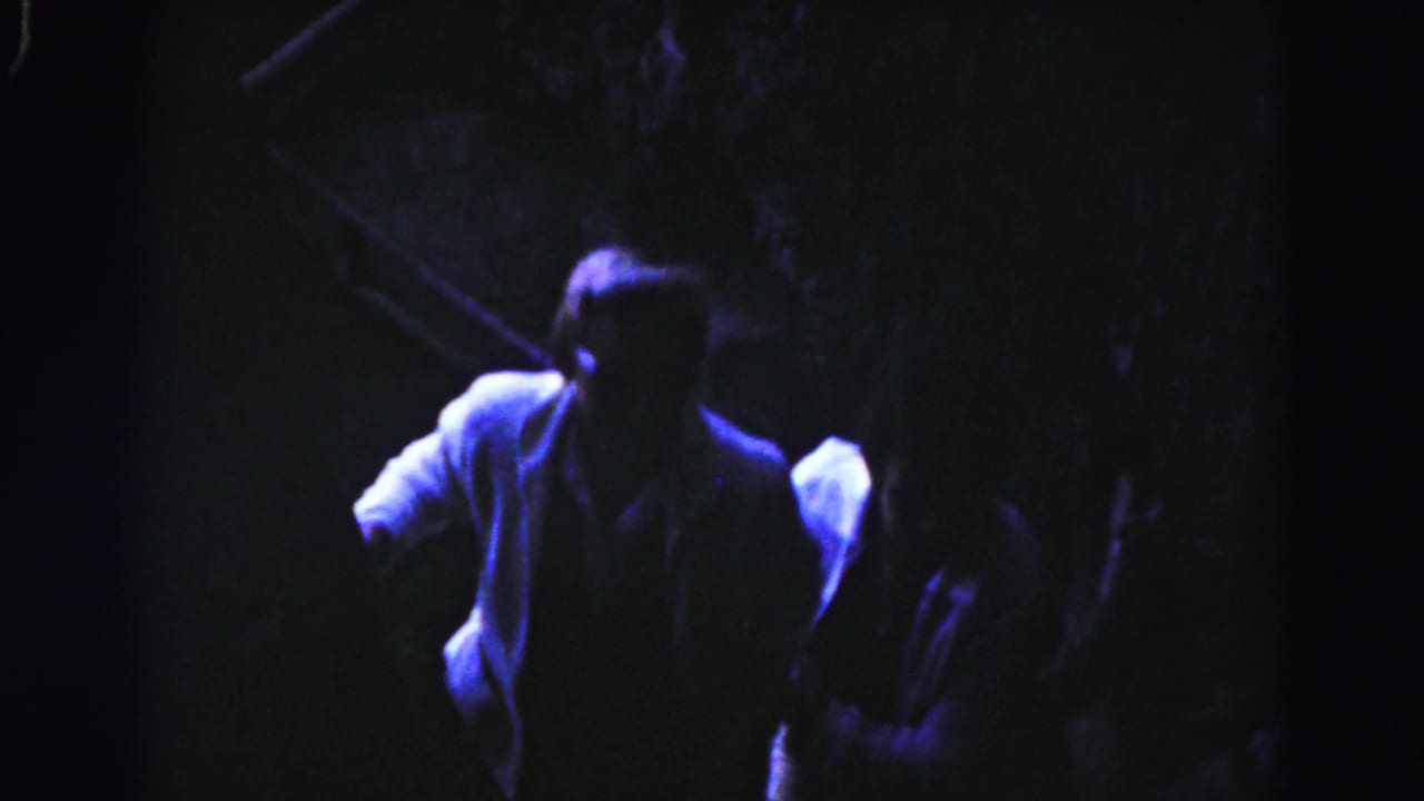 Two men partly visible on a dark stairway under blue-purple light.