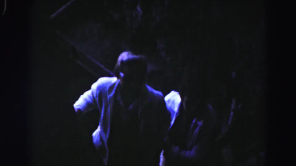 Two adult men ascend a dim stairway at night in 1963 Hagerstown home-movie footage, with one in a light jacket near the foreground.