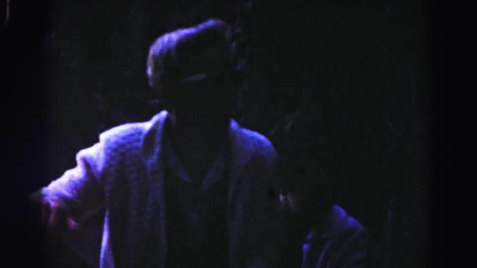 A light-jacketed man fills the dark frame near the top of the stairway, with another adult partly visible at the right edge.