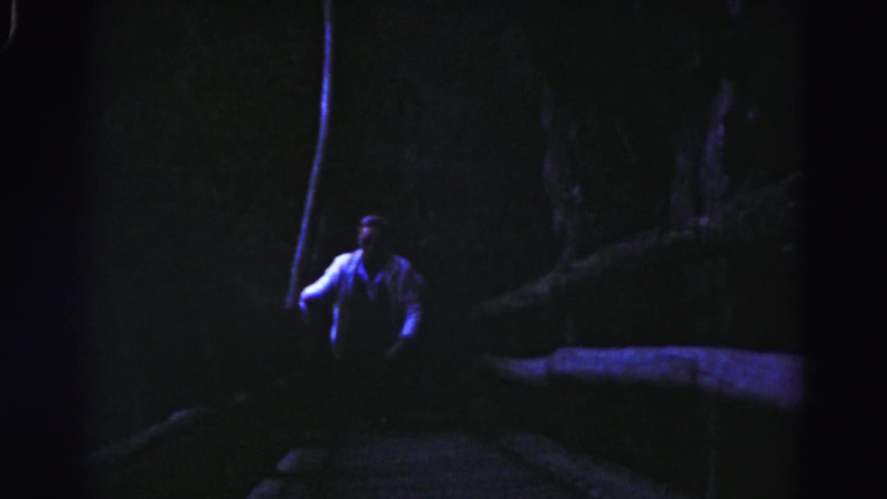 The man is seen farther up the nighttime staircase, with trees and a low wall or edge fading into shadow.
