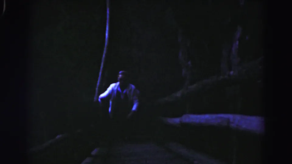 The man is seen farther up the nighttime staircase, with trees and a low wall or edge fading into shadow.