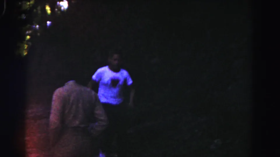 The closing 1963 8mm frame shows a blue-shirted person near the camera-facing edge while another figure remains in the wooded shade.