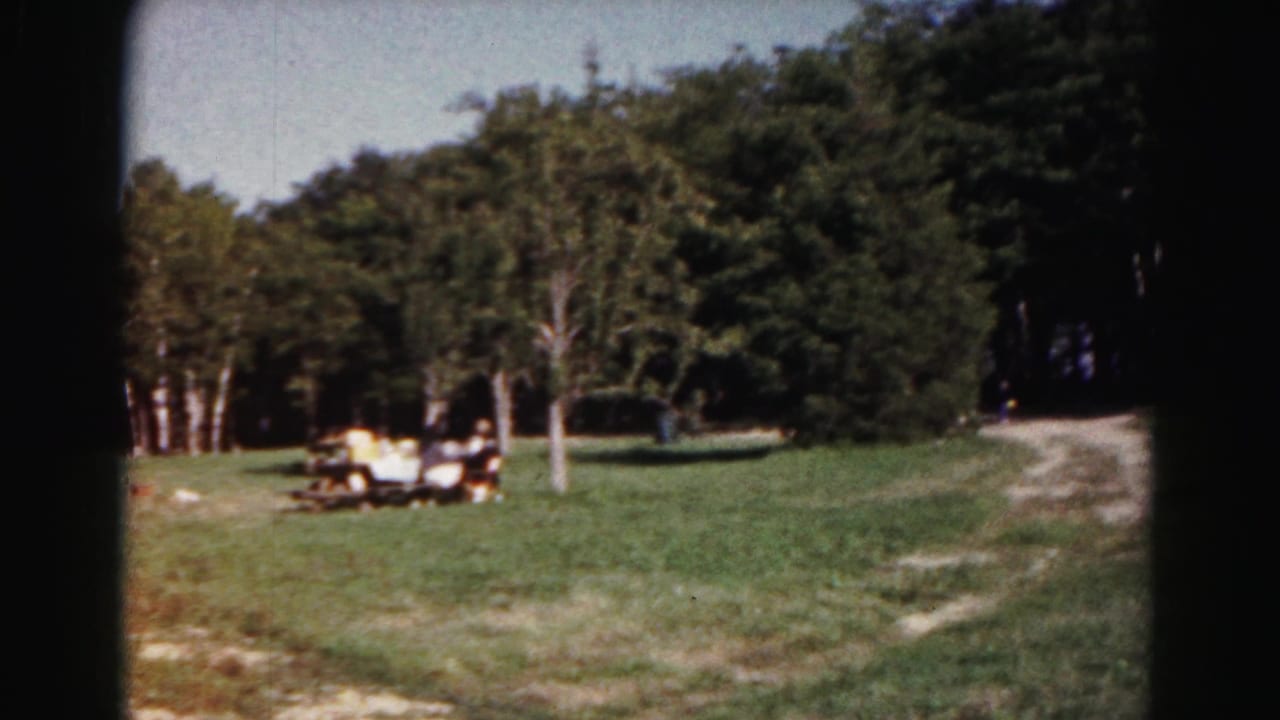 1963 Hagerstown park view with people near picnic tables on a grassy lawn beside trees and a dirt path.