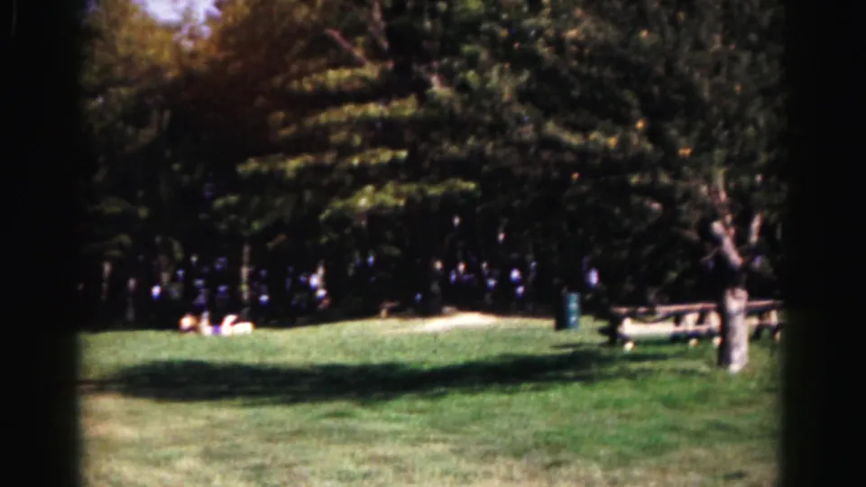 1963 Hagerstown park scene showing shaded grass, distant visitors, picnic tables, trees, and a dark trash can.