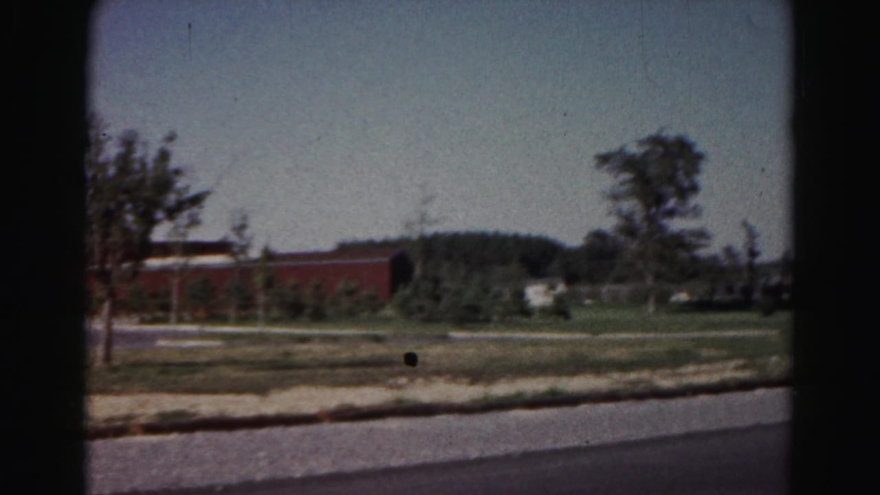 1963 Hagerstown roadside scene with a red brick building, young trees, open grass, and a paved road.