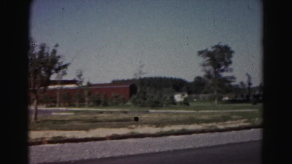 1963 Hagerstown roadside scene with a red brick building, young trees, open grass, and a paved road.