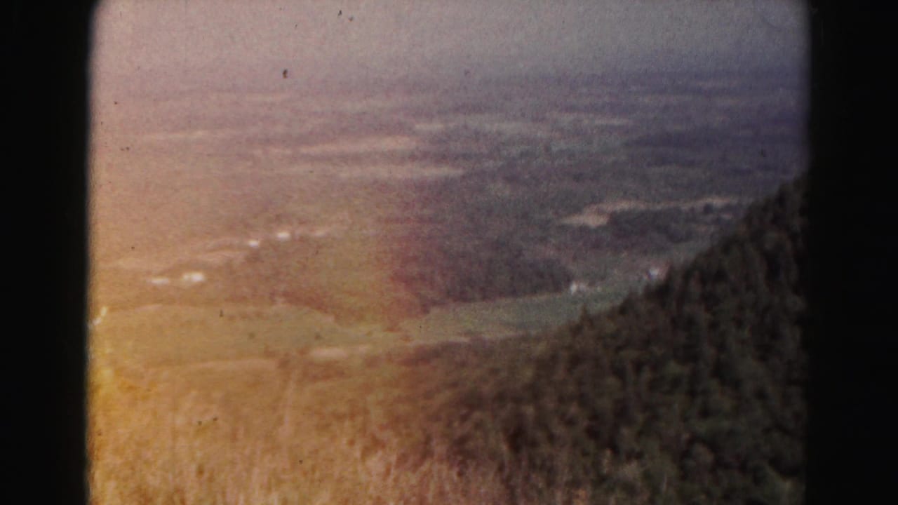 Hazy valley seen from a wooded mountain slope with dark film edges.