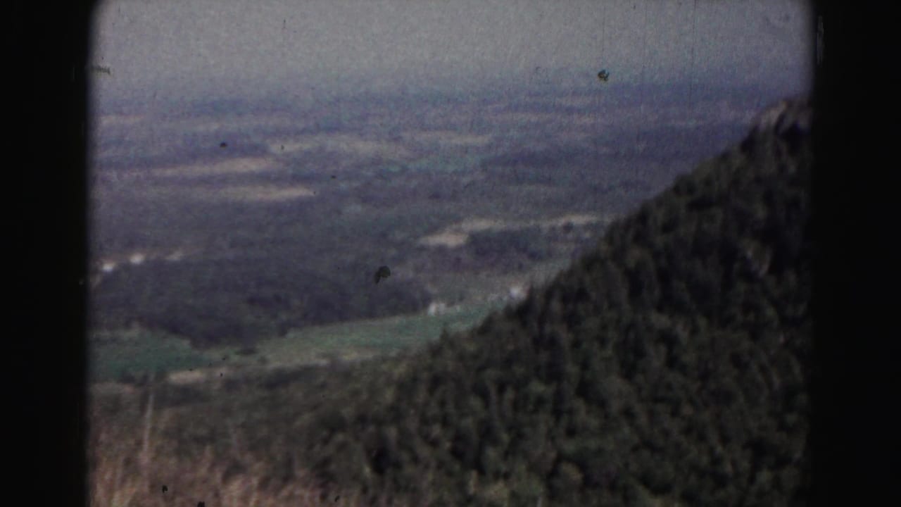 A 1963 Maryland mountain overlook frame shows a wooded ridge edge and distant valley floor under a muted, hazy sky.