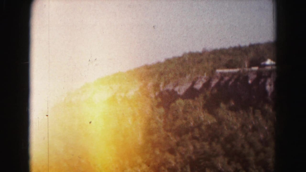 Wooded hill and valley view with strong yellow light leak at the left edge.