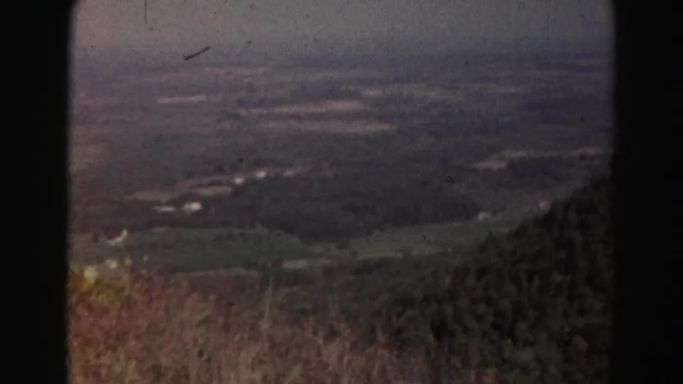 1963 Hagerstown-area 8mm frame of a hazy rural valley with fields and wooded land seen from an elevated overlook.