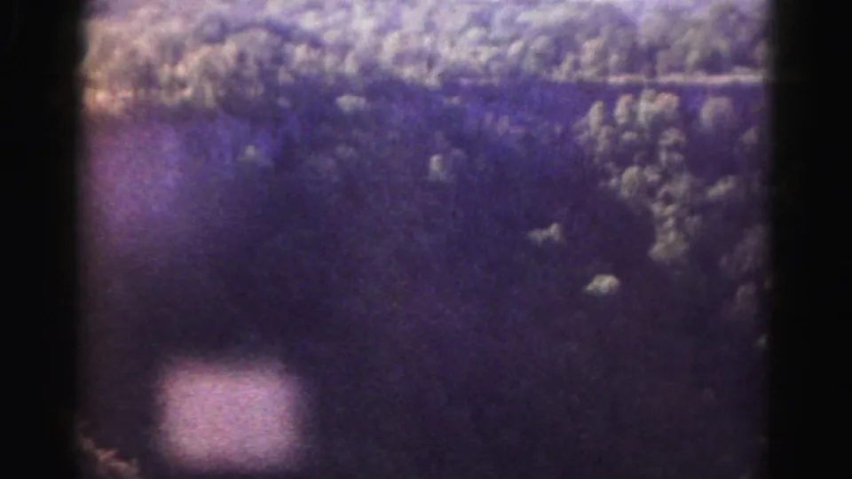 1963 Maryland home-movie frame showing a grainy aerial view across wooded hills and pale ridge-like textures.