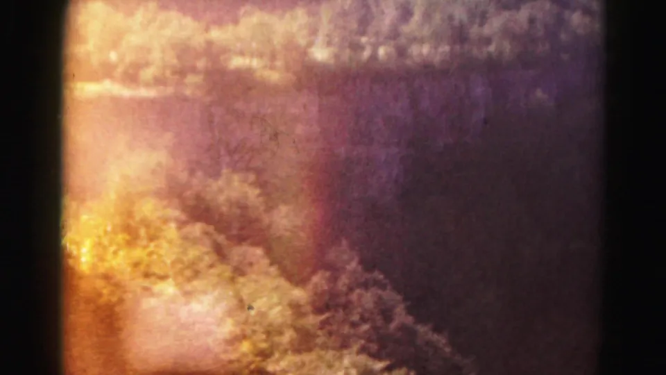A color-shifted 8mm frame shows a wooded or hillside landscape, with warm orange and purple tones from exposure or film aging.