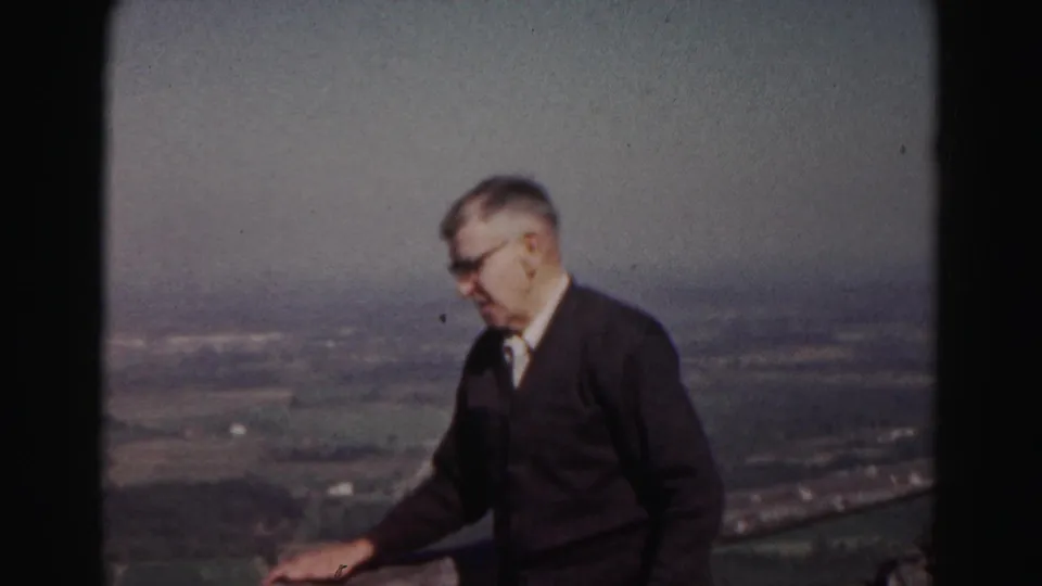 Older man in glasses and a dark sweater stands on a hilltop overlook near Hagerstown in 1963 home-movie footage.