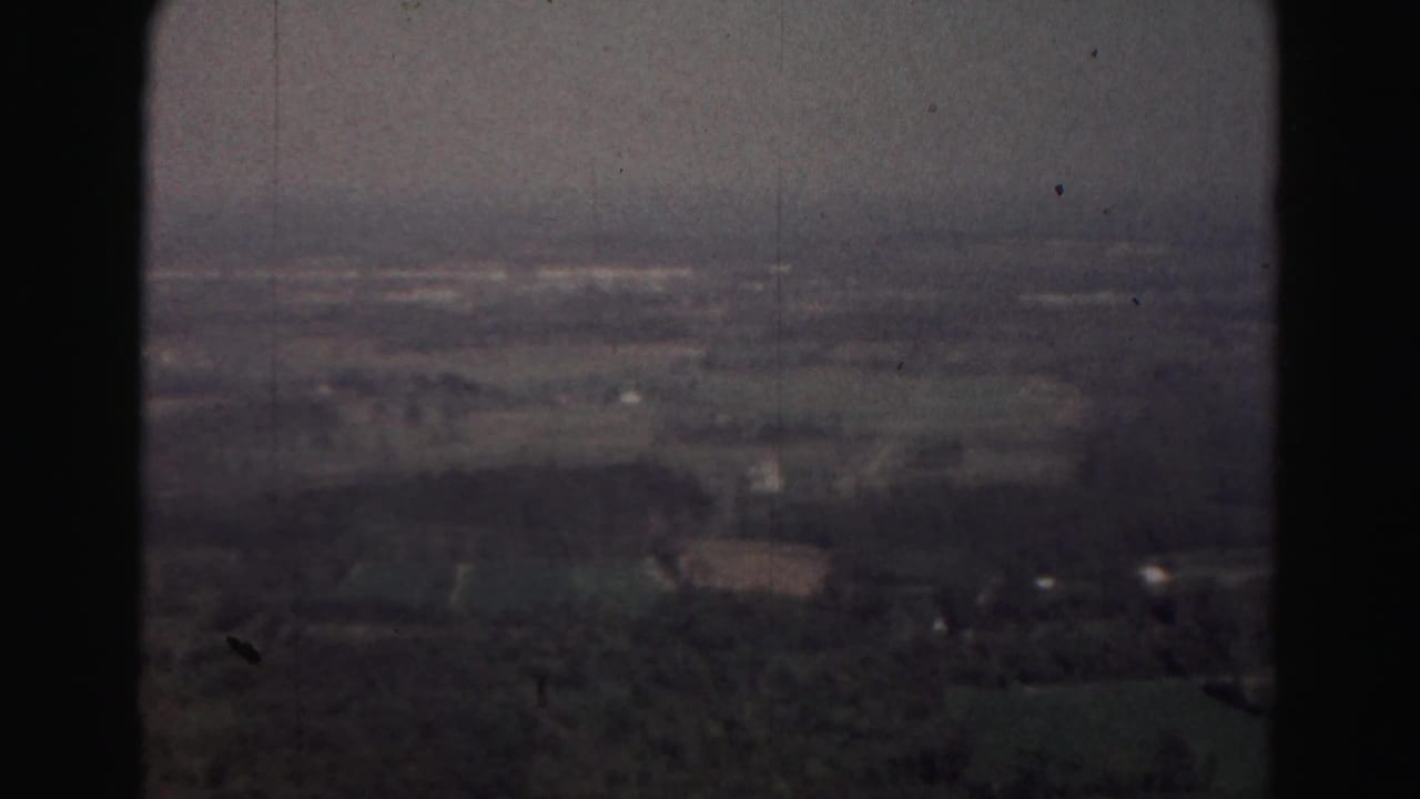 Distant rural landscape seen from above through a dark vertical window or film edge.