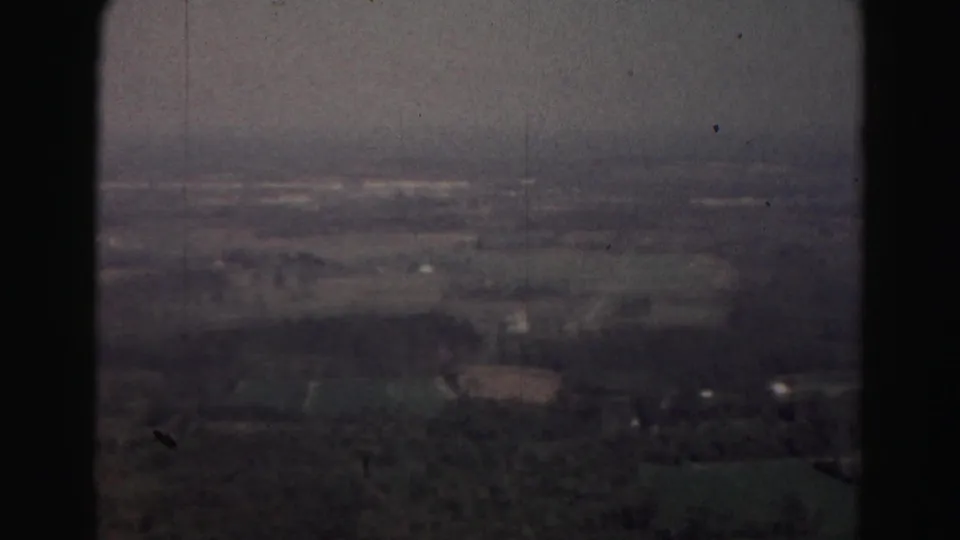 1963 8mm aerial view near Hagerstown, Maryland, showing hazy fields, tree cover, and scattered rural structures below.