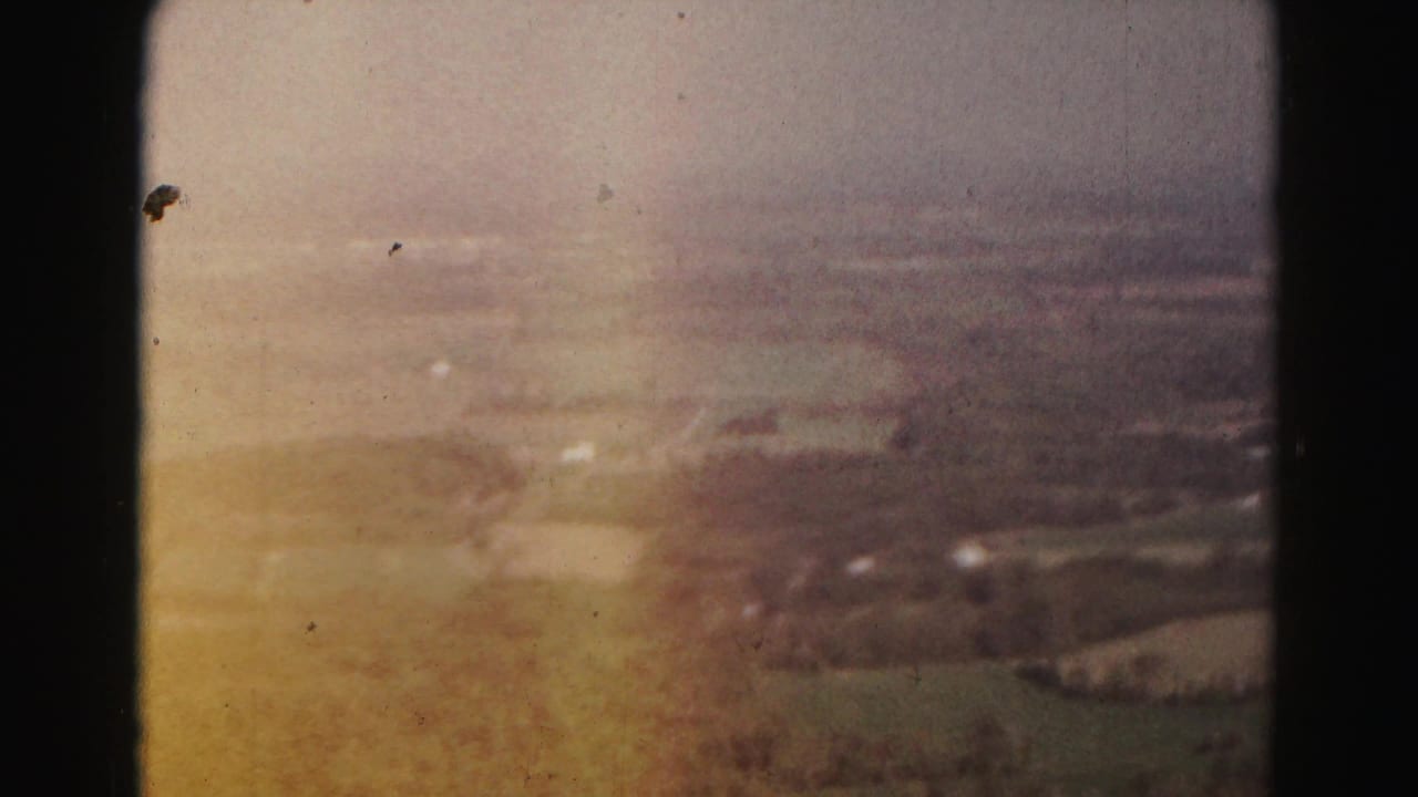 Warm-toned aerial view of fields and rural buildings through an airplane window.