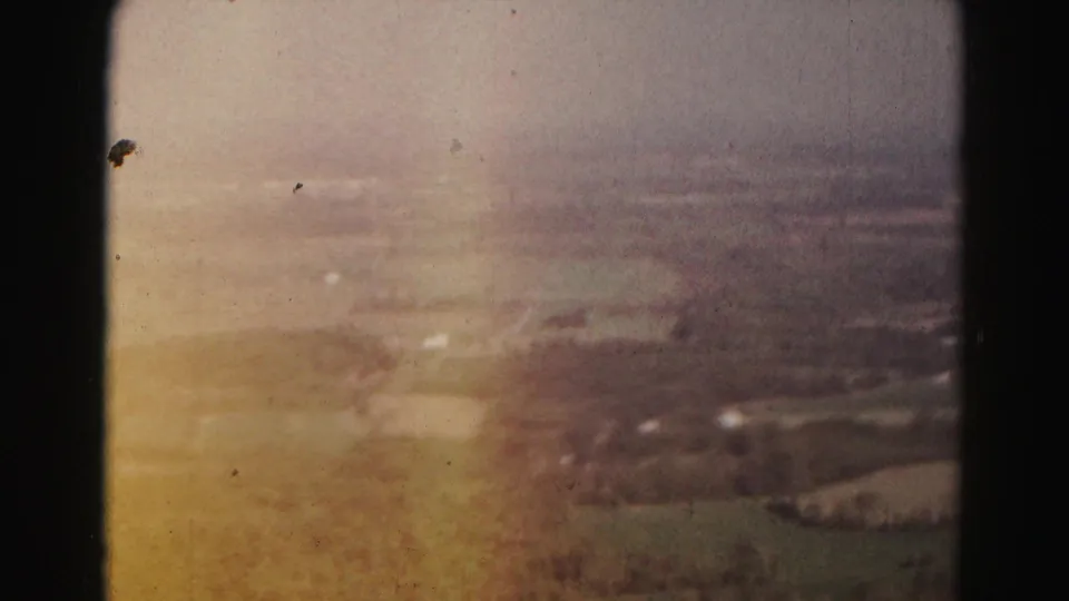 A warm, faded 1963 home-movie frame shows rural Maryland fields and scattered buildings from above.