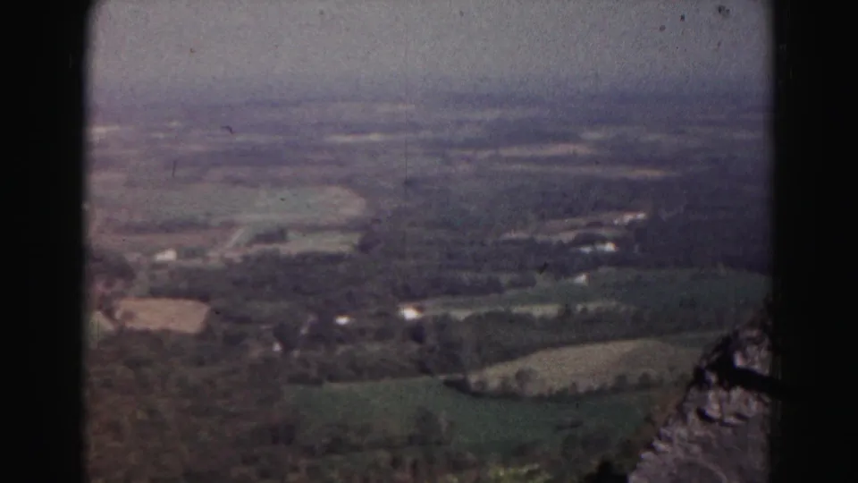 A 1963 8mm airplane view shows farmland, tree cover, rural buildings, and a hazy Maryland horizon.
