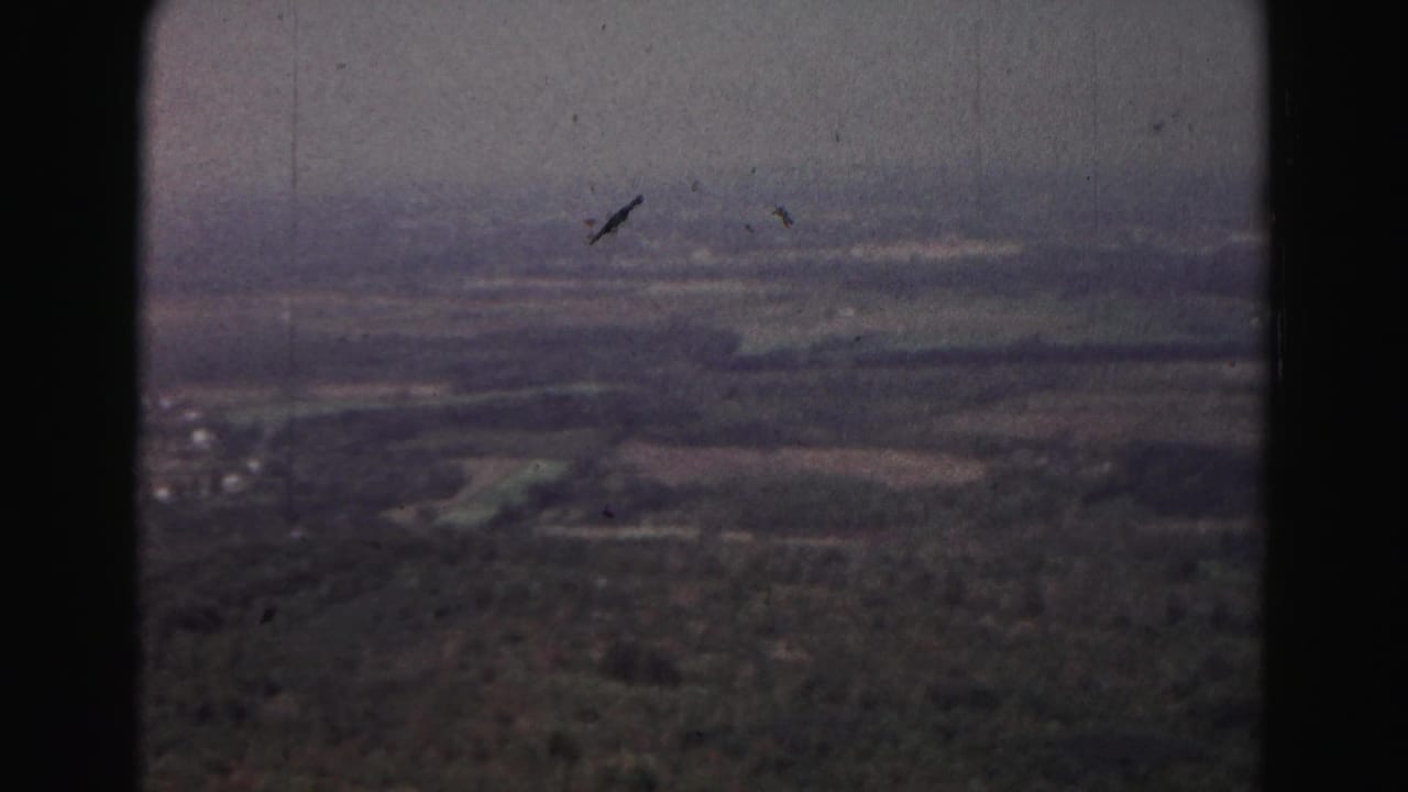 Hazy aerial view over fields and tree lines with distant rural settlement.