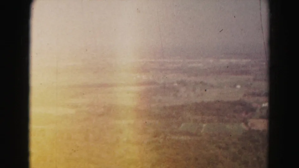 Warm-toned 1963 8mm frame over Hagerstown-area countryside, with fields softened by glare and haze.