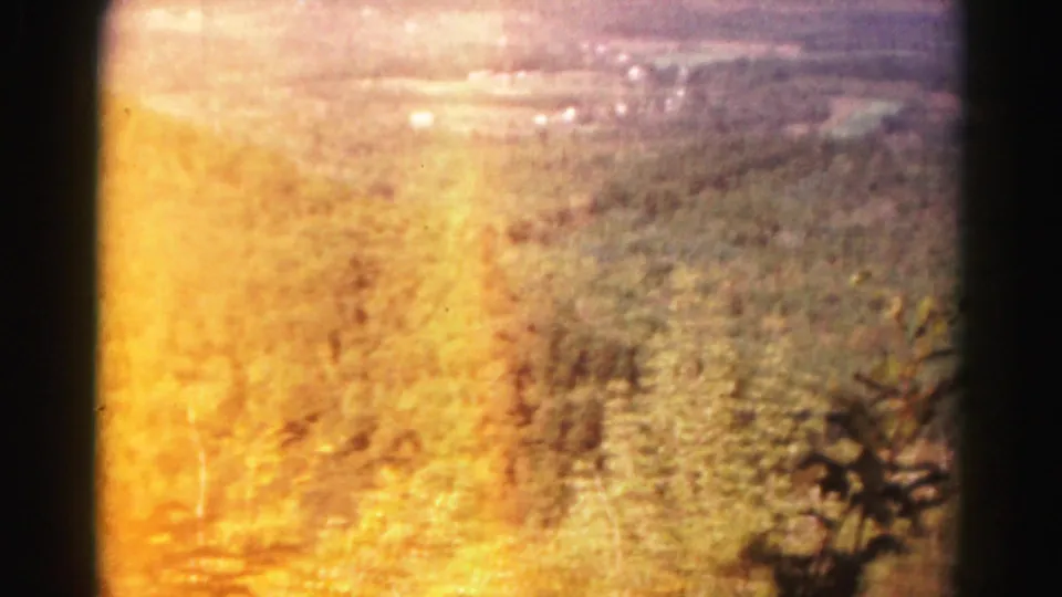 1963 home-movie frame looking across Maryland hills toward a distant valley, with strong yellow flare and soft focus.