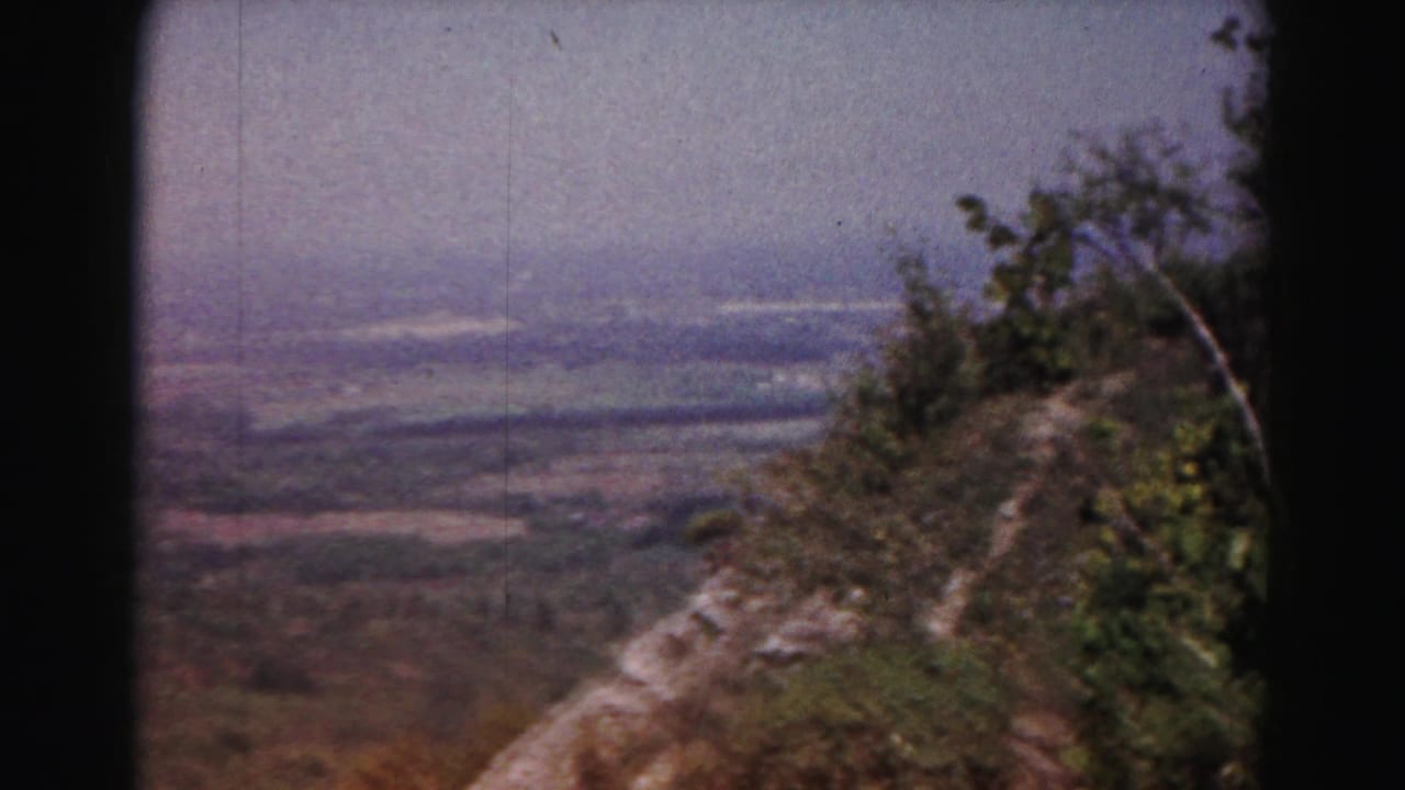 1963 Hagerstown-area 8mm view across a hazy valley, framed by trees and a rocky hillside edge.
