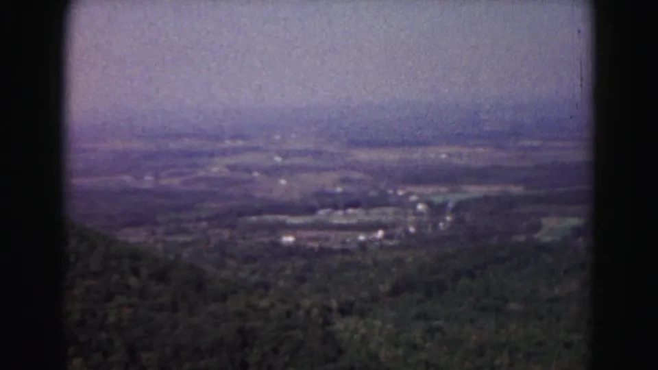 1963 Hagerstown-area home-movie view of a wooded valley, scattered buildings, and distant farmland under haze.